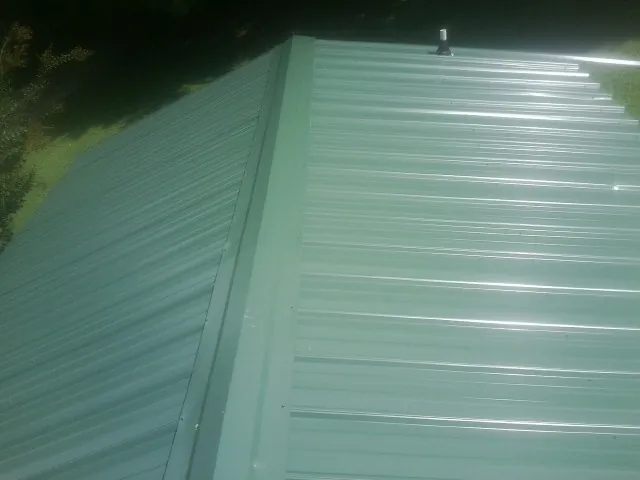 New green metal panels meeting at the ridge of a roof — Flat Roof Repair work by our crew in Ocoee
